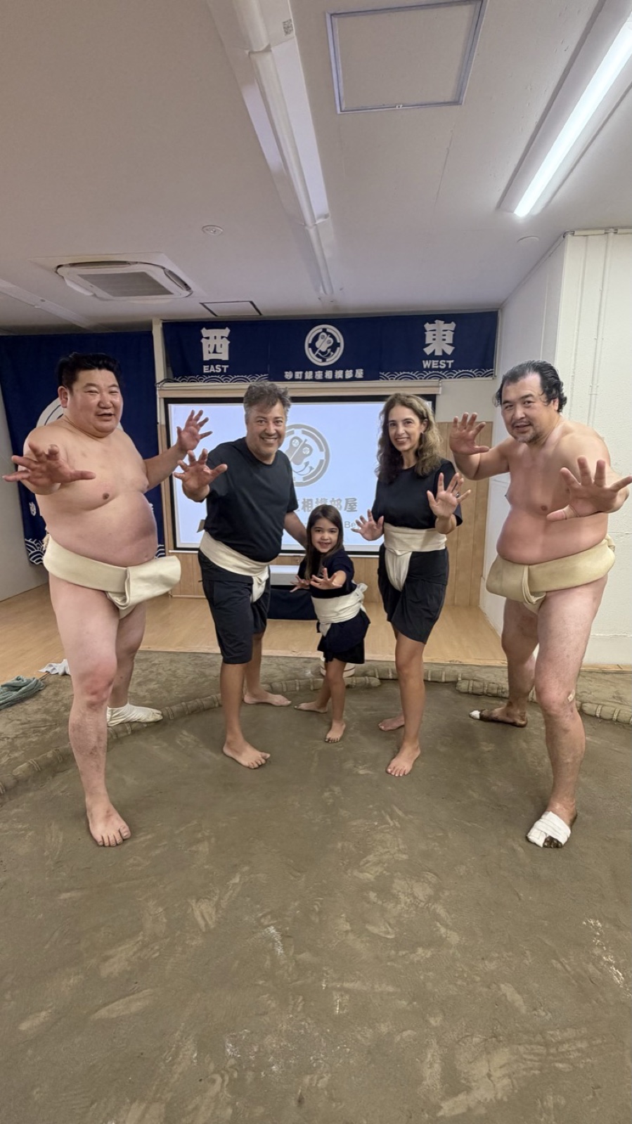 Two wrestlers and a family of three, the adults in practice mawashi, posing on the dohyo at the Sunamachi Ginza Sumo Stable